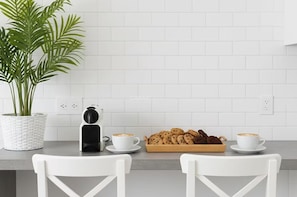 A modern kitchen with white tiled walls, a potted plant, a coffee maker, two cups of coffee, and a tray of cookies. - Sunny Apartment for 4 in Vera (Arona)