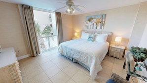 Quarto com uma cama grande, duas mesas de cabeceira com luminárias, um ventilador de teto e vista para o exterior através de uma porta de correr.