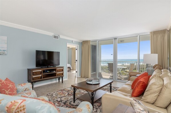 Een ruime woonkamer met een flatscreen-tv, comfortabele zitplaatsen, een salontafel en een grote schuifpui die uitkomt op een balkon met uitzicht op de oceaan.