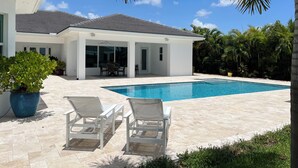 Ett modernt hus med en swimmingpool, vita utemöbler och en täckt uteplats.