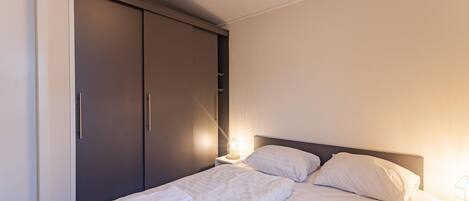 A hotel room with a bed, a wardrobe, and a nightstand.