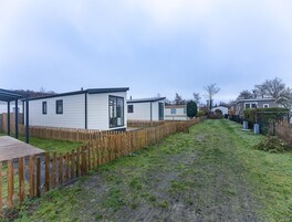 Una hilera de casas móviles con una valla de madera y un área verde al frente.