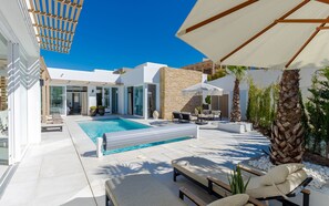 Een modern buitenzwembad met helderblauw water, ligbedden en een pergola voor schaduw.