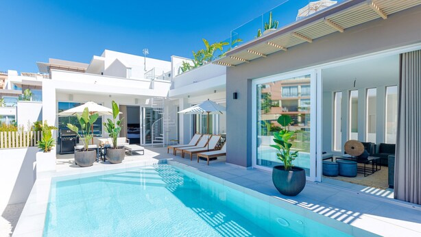 Ein moderner Poolbereich im Freien mit Liegestühlen und Sonnenschirmen, umgeben von Topfpflanzen und blauem Himmel.