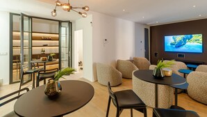 Ein modernes Wohnzimmer mit einem großen Flachbildfernseher, bequemen Sitzmöglichkeiten, einem Essbereich und einer Glastür zum Küchenbereich.