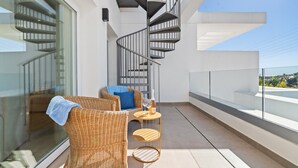 Ein Balkon mit Korbmöbeln, einer Wendeltreppe und einem Glasgeländer mit Blick auf eine Stadtlandschaft.