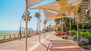 Eine Uferpromenade mit schattigen Bereichen, Palmen und Blick auf den Strand.