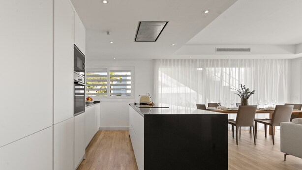 Una cocina moderna con armarios blancos, una isla negra y una zona de comedor con mesa y sillas de madera.
