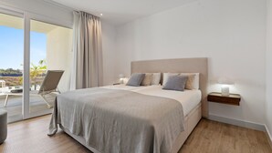 Un dormitorio moderno con una cama grande, una mesita de noche y una silla junto a un ventanal corredero que da a un balcón.