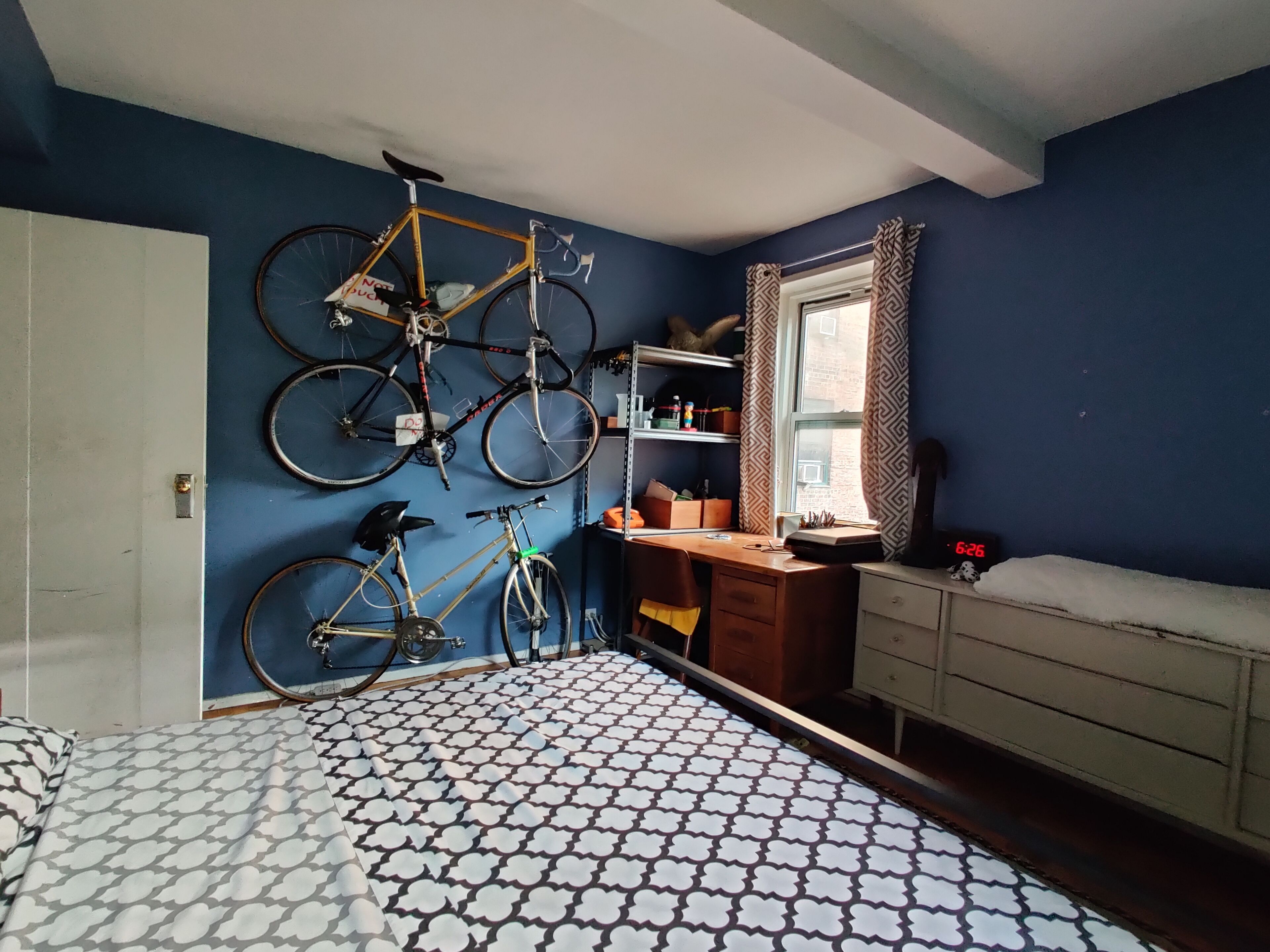 Une chambre avec un sol à motifs, un bureau, une chaise, un lit et deux vélos accrochés au mur.