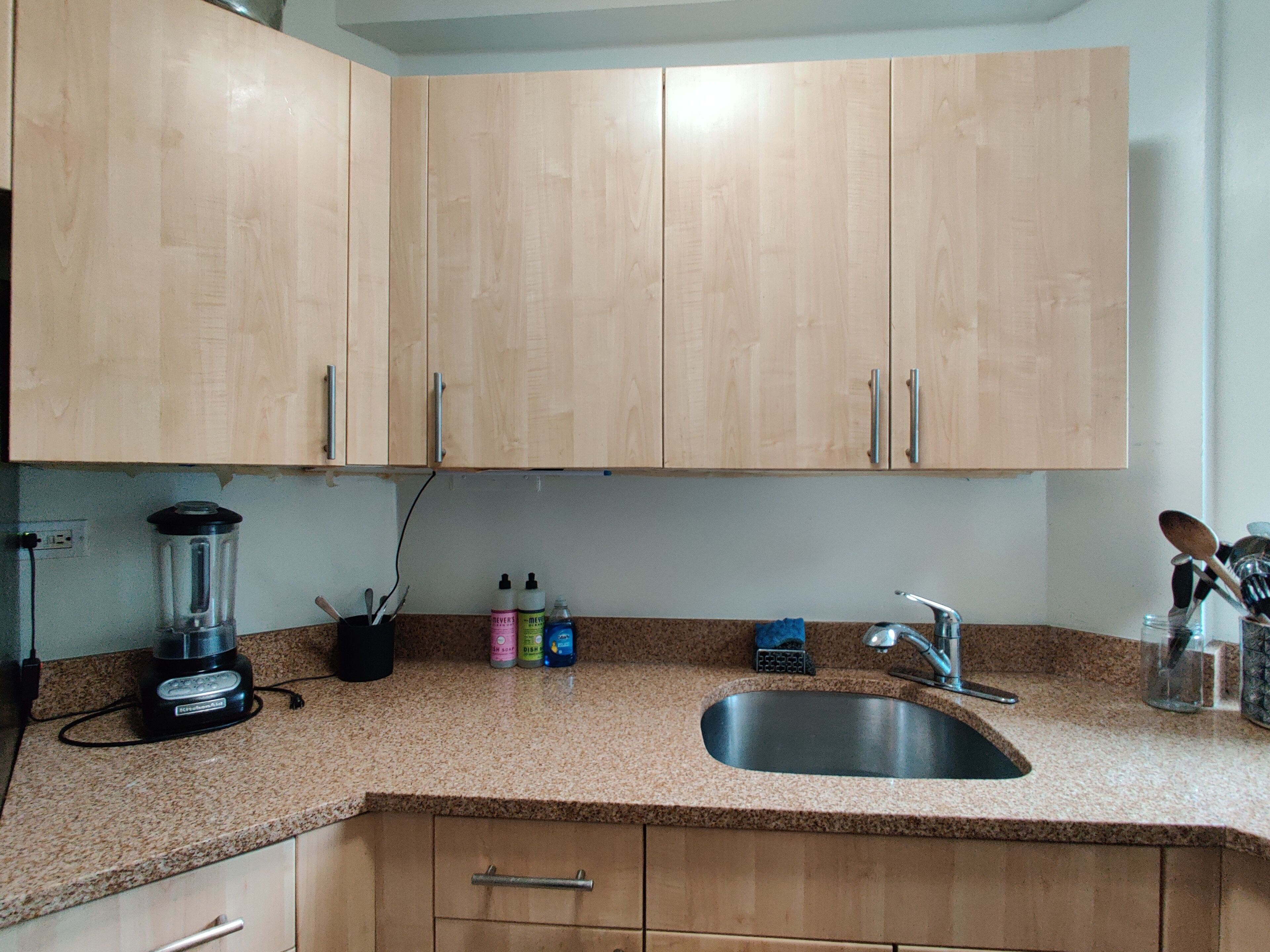 A kitchen with wooden cabinets, a granite countertop, a blender, a sink, and various kitchen utensils.