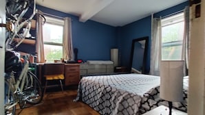 Un dormitorio con cama, escritorio, silla, bicicleta y ventana con cortinas.