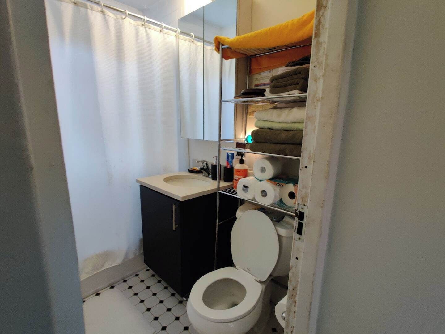 Un baño pequeño con inodoro, lavamanos y estantes con toallas y artículos de aseo.
