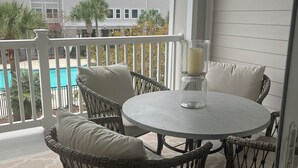 A balcony with wicker chairs and a round table, overlooking a swimming pool and a building with multiple windows. - Delightful 2-bedroom renovated condo with AC in charming Charleston (Charleston)