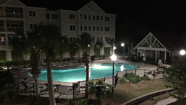 A nighttime view of a hotel with a swimming pool surrounded by palm trees and a fenced deck area. - Delightful 2-bedroom renovated condo with AC in charming Charleston (Charleston)