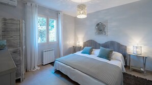 Et soveværelse med en seng, to sengeborde, en radiator, et vindue med gardiner, en loftlampe og et billedværk på væggen.