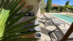 Et overdækket udendørs opholdsområde med pool, liggestole og et mønstret tæppe.
