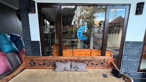 A wooden sofa with cushions, a glass door, and a tiled floor. - Q-Star Uluwatu (Ungasan)