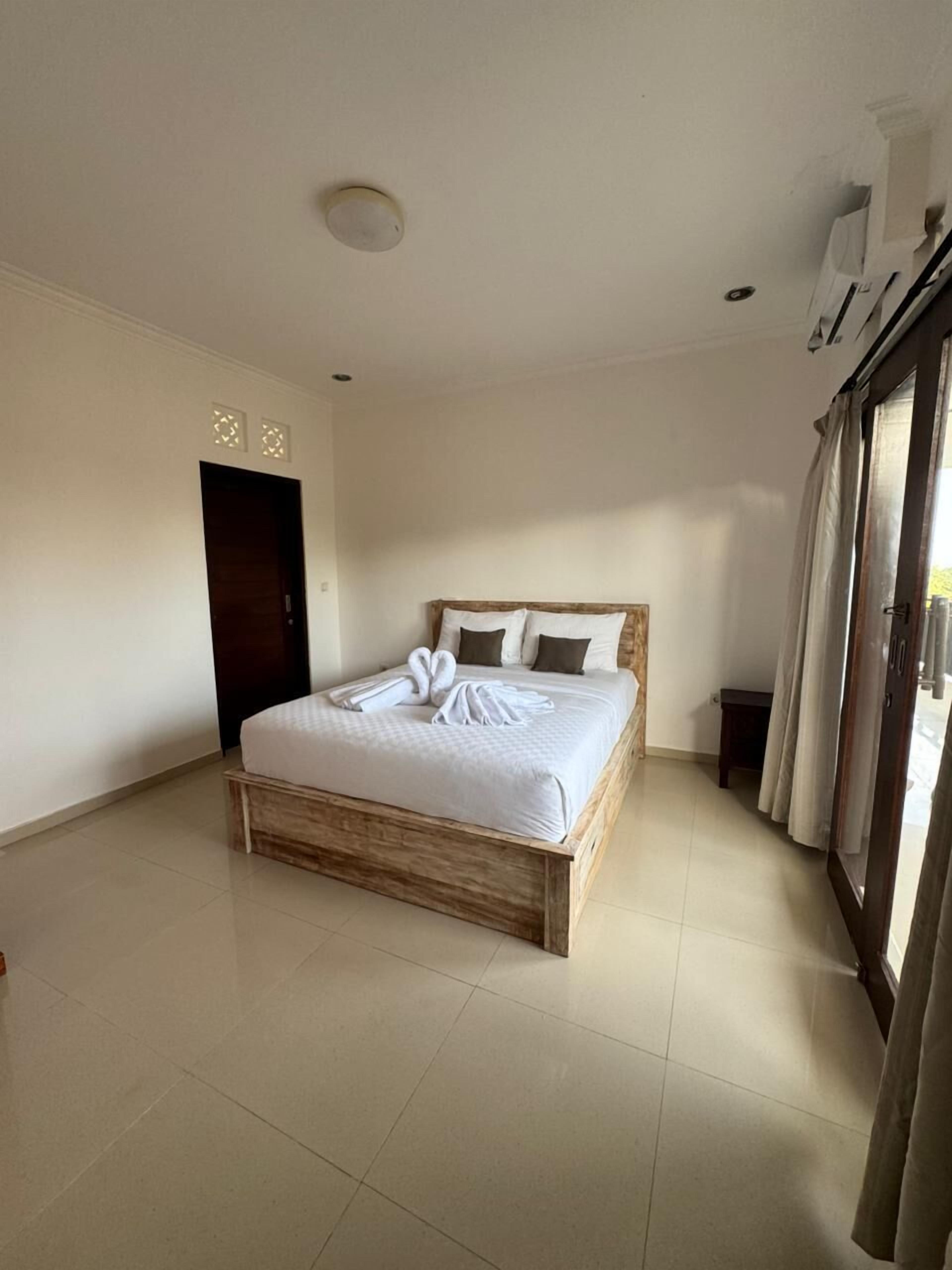 Un dormitorio con cama de madera, una puerta oscura, una mesita de noche pequeña y una ventana con cortinas.