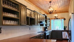 Una cocina con techo de madera, una isla central con taburetes y un refrigerador.