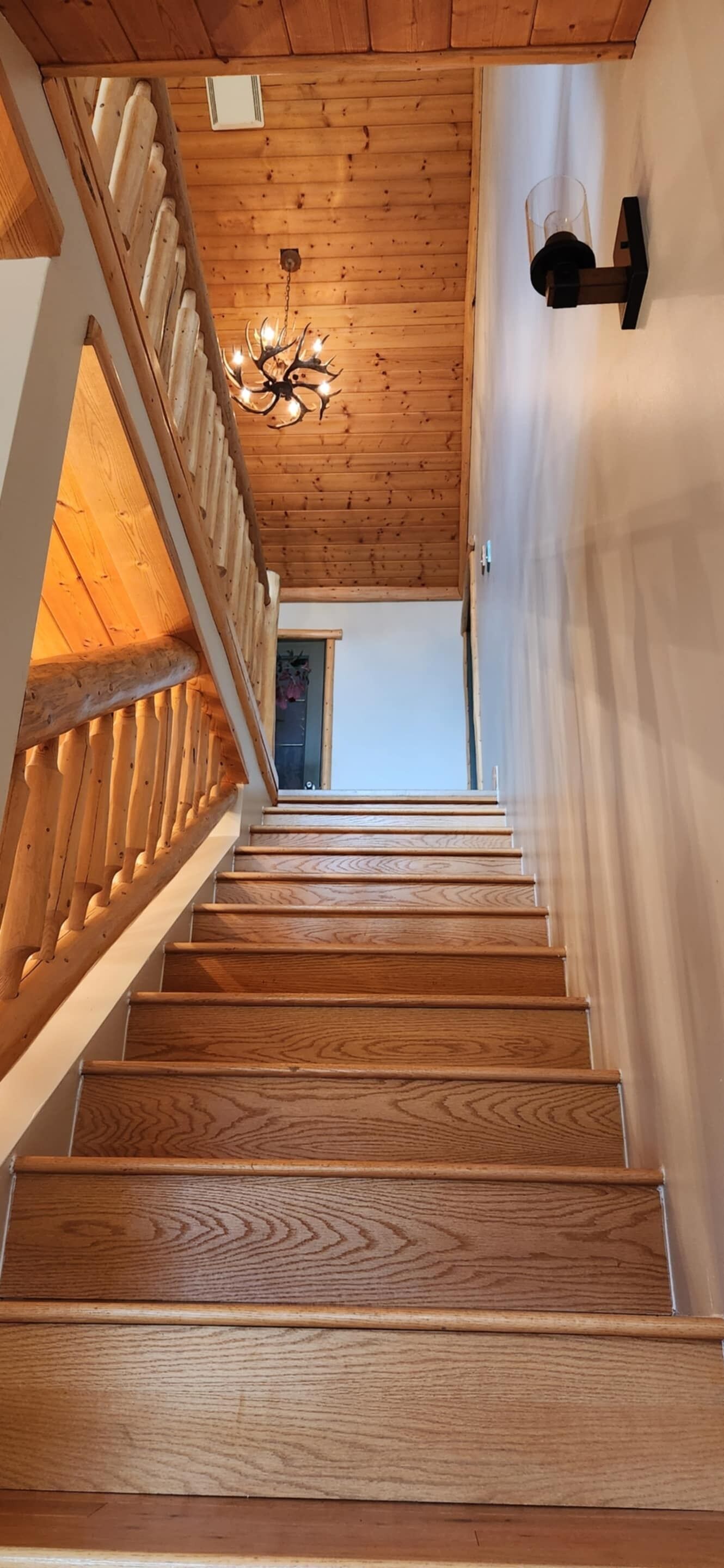 Una escalera de madera con barandilla, un candelabro y una lámpara fijada a la pared.