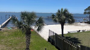 A beach with a wooden pier, palm trees, and a clear blue sky.