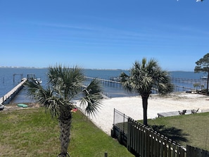 A beach with a wooden pier, palm trees, and a clear blue sky.