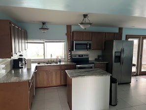 A kitchen with wooden cabinets, a stainless steel refrigerator, a microwave, an oven, and a sink.