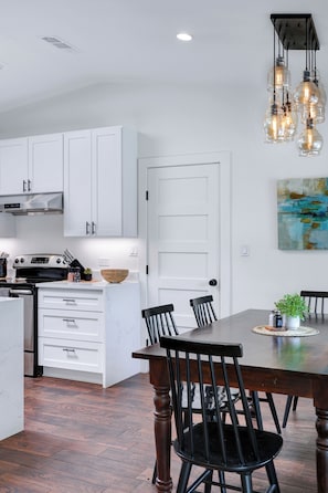 A modern kitchen with white cabinets, a wooden dining table, and black chairs. - Spacious, 4-bedroom house with private pool in a walkable location. (San Antonio)