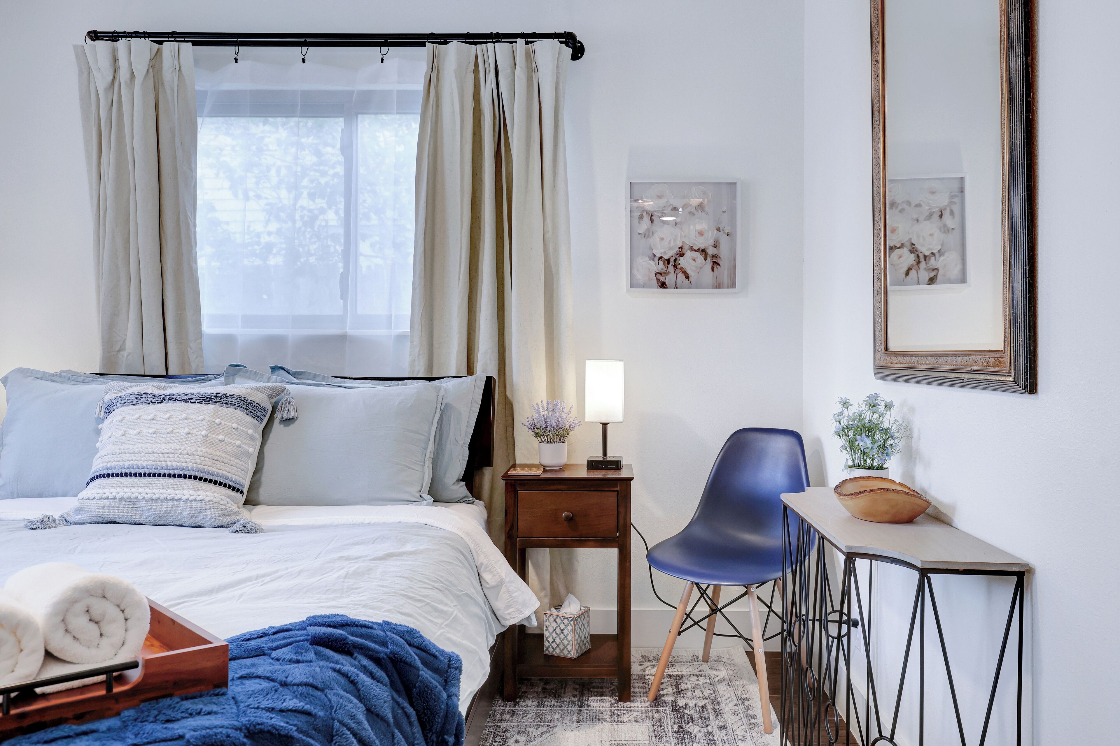 Ein ordentlich eingerichtetes Schlafzimmer mit Bett, Nachttisch, Stuhl und kleinem Schreibtisch.