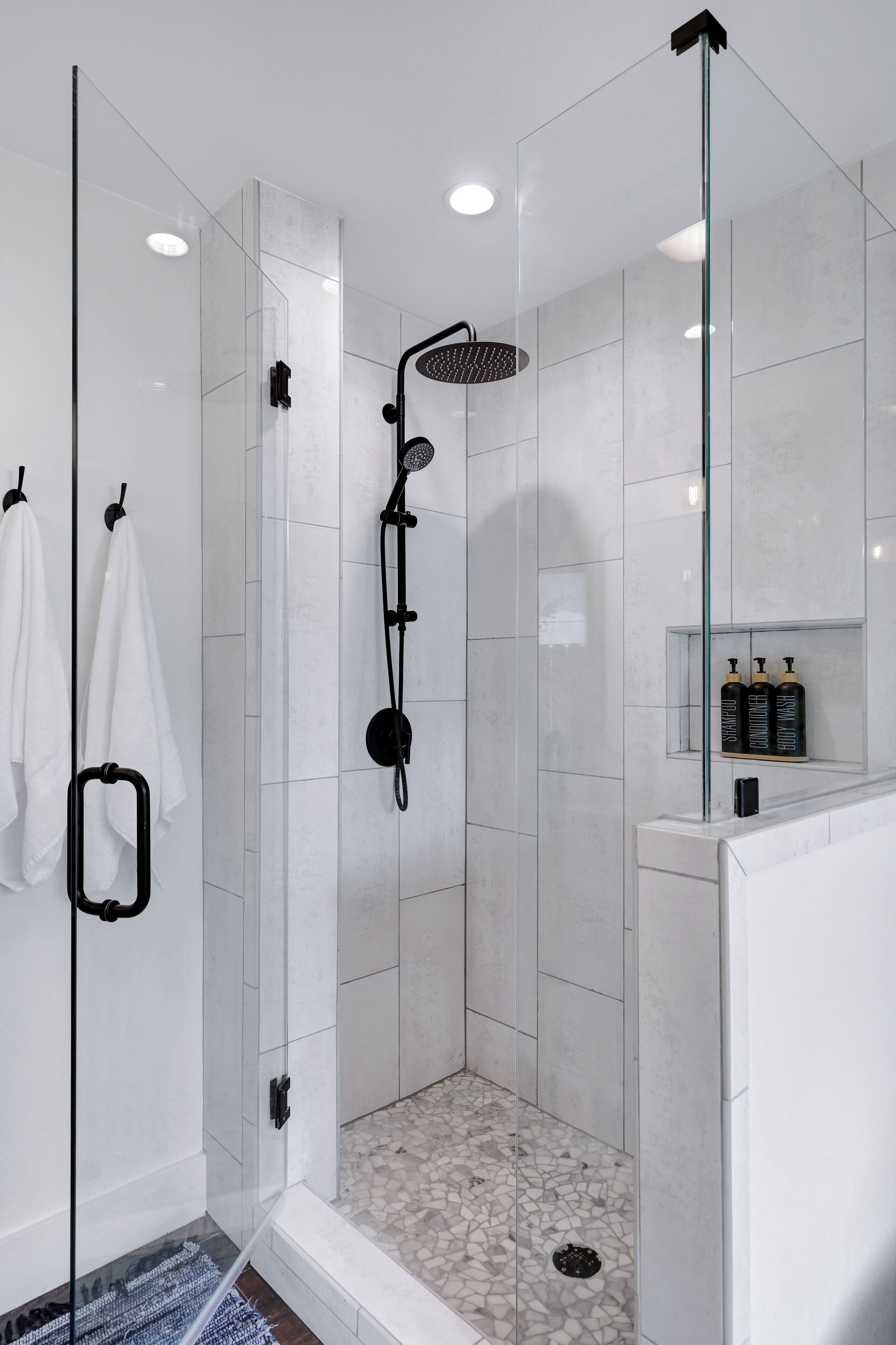 Uma área de chuveiro moderna com porta de vidro, chuveiro manual e piso revestido com azulejos.