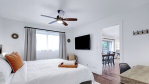 Et soveværelse med seng, ventilator, fjernsyn og et spiseområde med stole og bord.