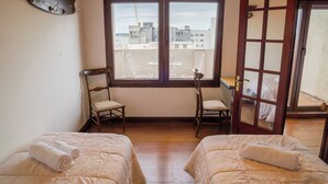 A room with two beds, a window with a view of buildings, a chair, and a coat rack. - Penthouse with two terraces at the Old City [502]. (Montevideo)