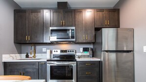 Una cocina moderna con gabinetes de madera oscura, electrodomésticos de acero inoxidable, incluyendo un microondas, horno y refrigerador, y una encimera de mármol.