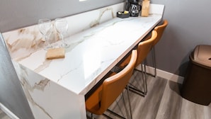 Una cocina con encimera de mármol, dos copas de vino, una cafetera y un cubo de basura.