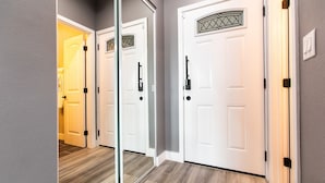 Un pasillo con dos puertas blancas, una con un panel de vidrio y la otra con un vidrio decorativo. El suelo es de madera y las paredes están pintadas de gris.