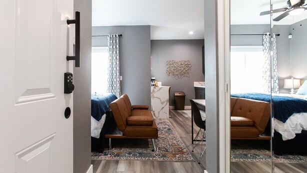Una habitación de hotel moderna con una cama, dos sillones marrones, una mesita y un espejo.