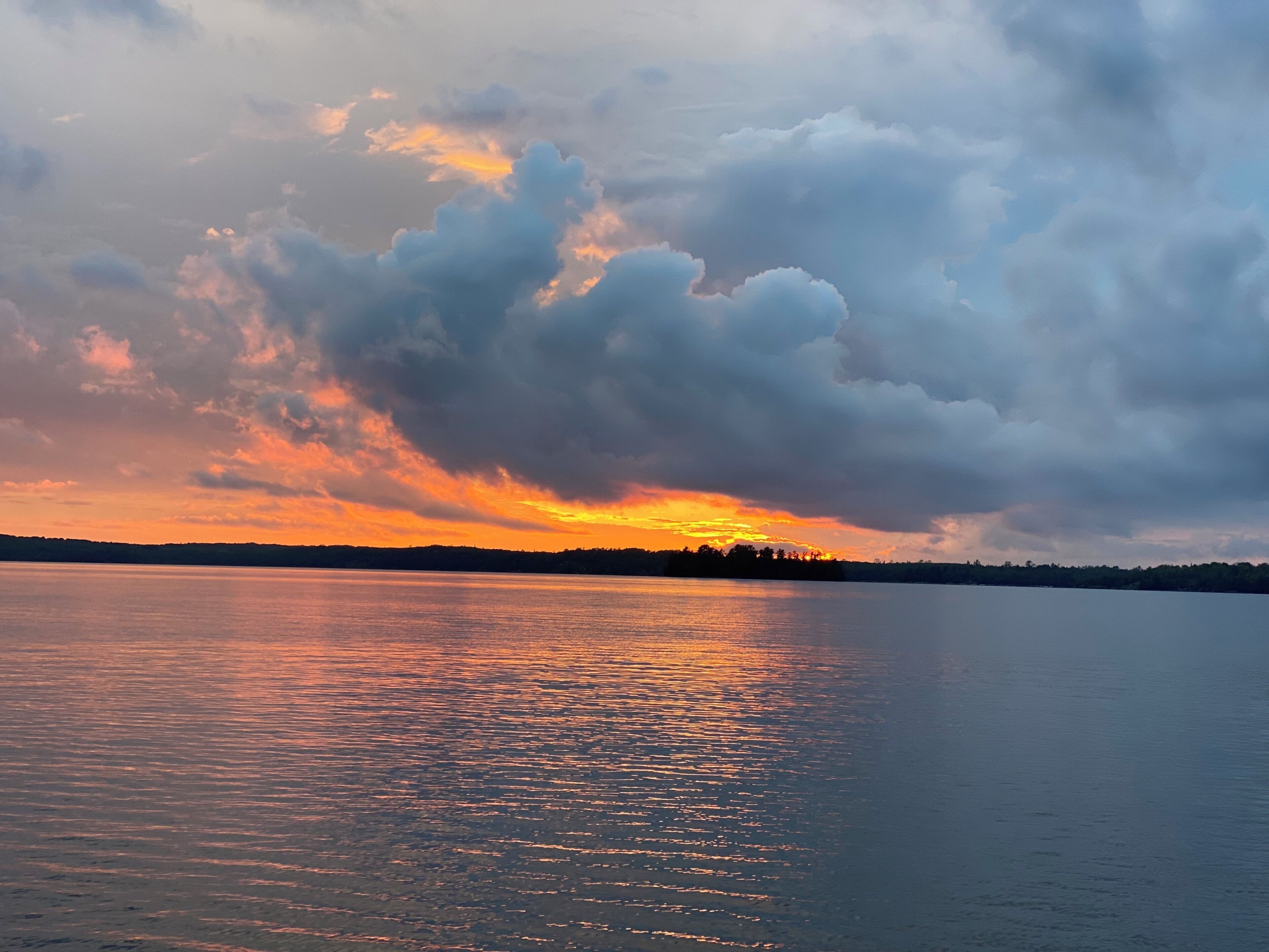 A sunset over a calm lake with a silhouette of trees on the horizon.