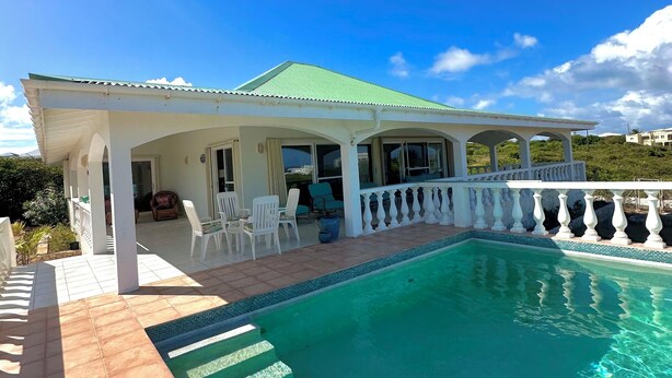Una casa con piscina, un patio cubierto con sillas y vistas del paisaje circundante.