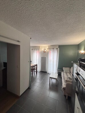 A compact living space with a kitchenette, a dining area, and a seating area with a sofa and a small table. - Downtown Apartment Near the Cable Car   (Cauterets)