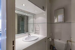 Ein modernes Badezimmer mit einem weißen Waschbecken, einem großen Spiegel und einer Toilette.