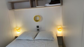 Una cama con ropa de cama blanca, dos lámparas de noche, un espejo circular en la pared y una repisa sobre la cama.