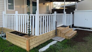 Una casa con porche cubierto, cerca blanca y jardines elevados.
