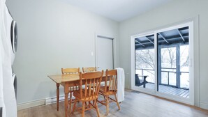 Un comedor con una mesa y sillas de madera, una puerta y un amplio ventanal corredera que da a una terraza exterior.