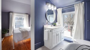 Un baño con tocador blanco, espejo redondo y ventana con cortinas.