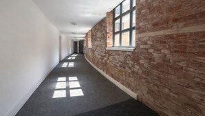 Ein Gang mit einer Backsteinwand an einer Seite und einer weißen Wand an der anderen, der zu einer Tür am Ende führt.