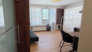 Habitació moderna amb sòl de fusta, una banca, taula de dinar amb cadires i finestra amb cortines.