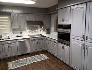 A kitchen with grey cabinets, a stainless steel dishwasher, a built-in oven, and a tiled backsplash. - Tranquil 2-bedroom next to Remington Park, conveniently close to Loop 289 (Lubbock)