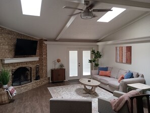 A living room with a fireplace, a ceiling fan, a flat-screen TV, a sofa, and a coffee table. - Tranquil 2-bedroom next to Remington Park, conveniently close to Loop 289 (Lubbock)
