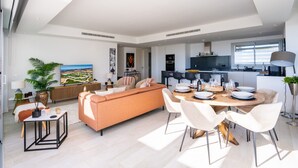 A modern living room with a sofa, dining table, and chairs. There is a kitchen area with appliances and a window. - Apartment Stay at Alcazaba Lagoon (Casares)